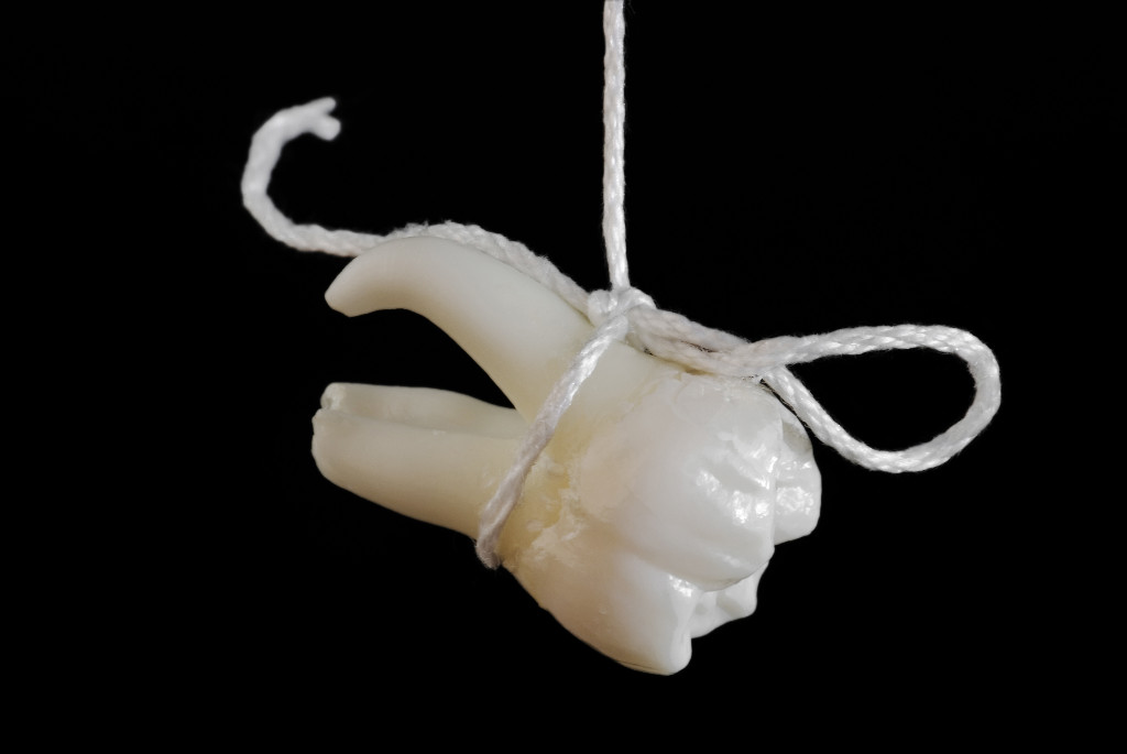 Tooth extracting method. Real human tooth hanging on thread